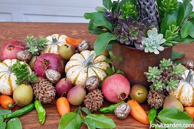 Small-pears-white-and-orange-pumpkins-pomegranates-orange-peppers-green-peppersmagnolia-cones-ans-gilded-walnuts-are-next-to-a-brass-pot-with-succulents-fall-table-decoration.jpg